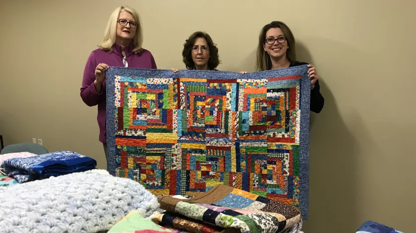 Tammie Ryan, RN, Shirley MacLeod of Thimbles and Friends, and Lisa Royer pose with a quilt